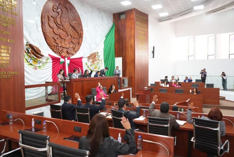 Diputados en sesión en la sede del Congreso de Tlaxcala, con miembros levantando la mano durante un debate o votación.