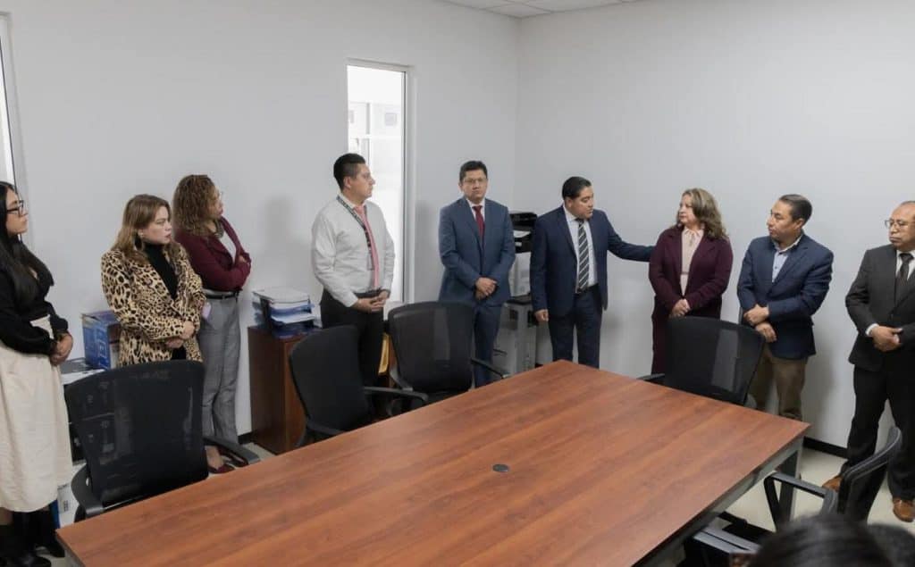 Conferencia de prensa en la que varios funcionarios y servidoras públicas participan en una reunión formal en una sala de reuniones moderna y sencilla.