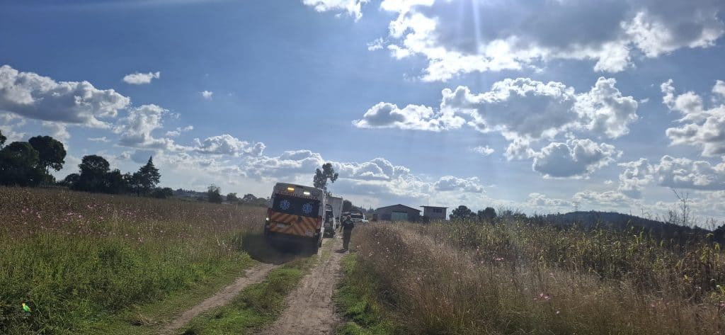 Ambulancias en una carretera rural rodeada de campos y cielo nublado, atendiendo una emergencia en Tlaxcala, México. Rescatistas trabajan en una zona alejada, con un entorno natural y cielo parcialmente cubierto de nubes.