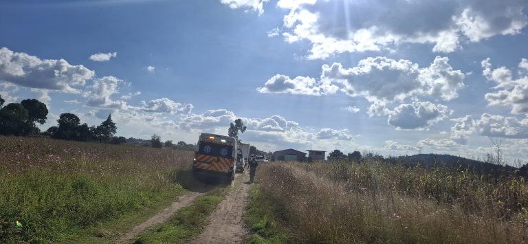 Ambulancias en una carretera rural rodeada de campos y cielo nublado, atendiendo una emergencia en Tlaxcala, México. Rescatistas trabajan en una zona alejada, con un entorno natural y cielo parcialmente cubierto de nubes.