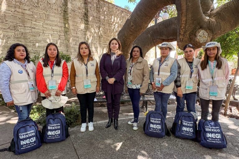 Personal de INEGI en una actividad al aire libre frente a un árbol grande, con bultos y gafetes de identificación, participando en una tarea relacionada con censos o encuestas.