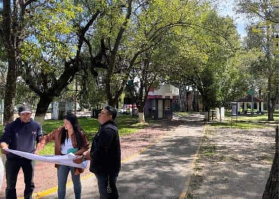 Edificio de oficinas en un parque con árboles y personas revisando planos, en Tlaxcala, México.
