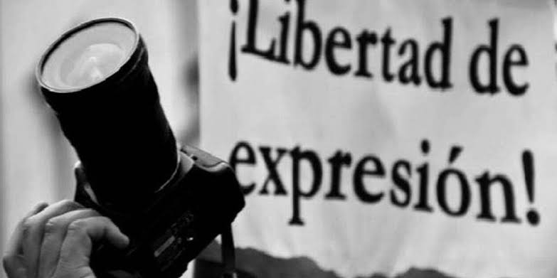 Fotografía en negro y blanco que muestra una cámara fotográfica y un cartel que dice "¡Libertad de expresión!". La imagen simboliza la importancia de la libertad de prensa y el derecho a la expresión.