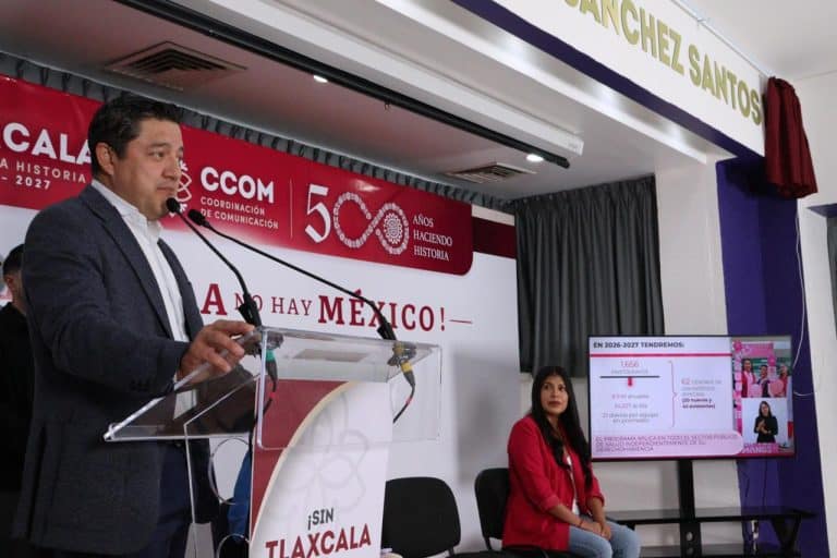 Archivo de prensa en donde un hombre da un discurso en un evento con un banner rojo y gráficos en una sala de conferencia en Tlaxcala.