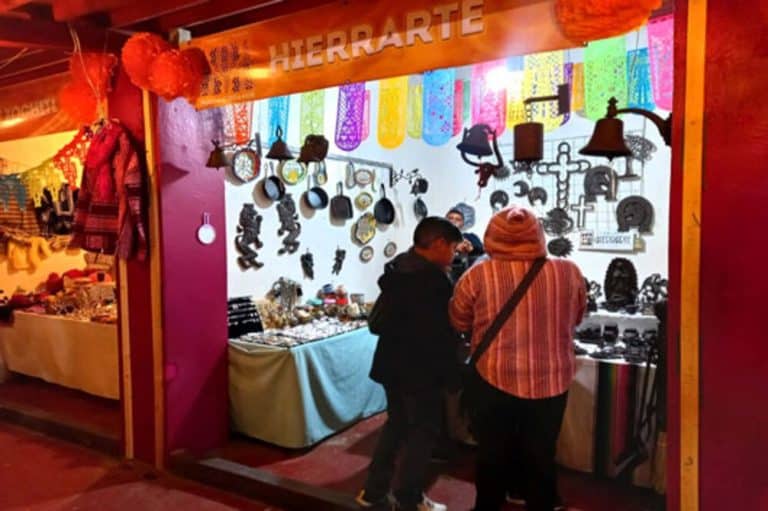 Colorful Mexican handicraft stall at a local market with ornaments, jewelry, and decorations displayed on tables and hanging on the wall.