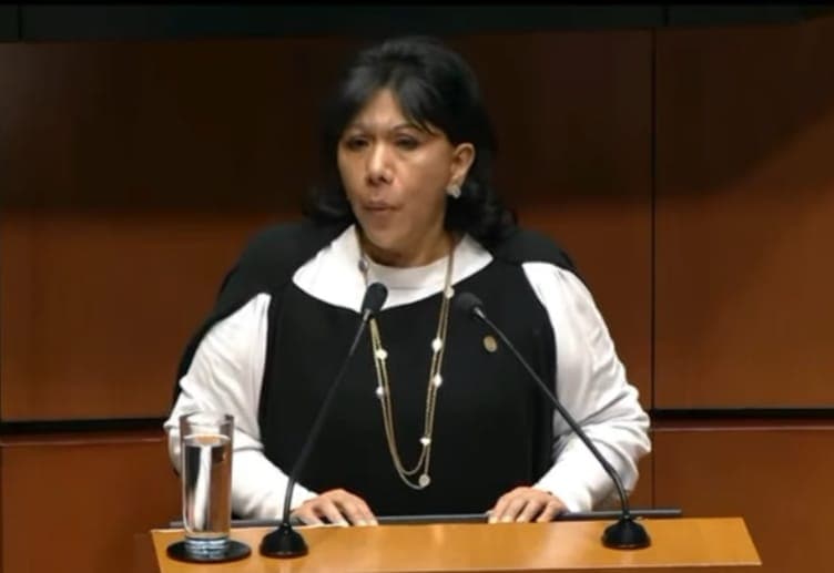 Losada hablando en un escenario, con micrófonos y un vaso con agua frente a ella.