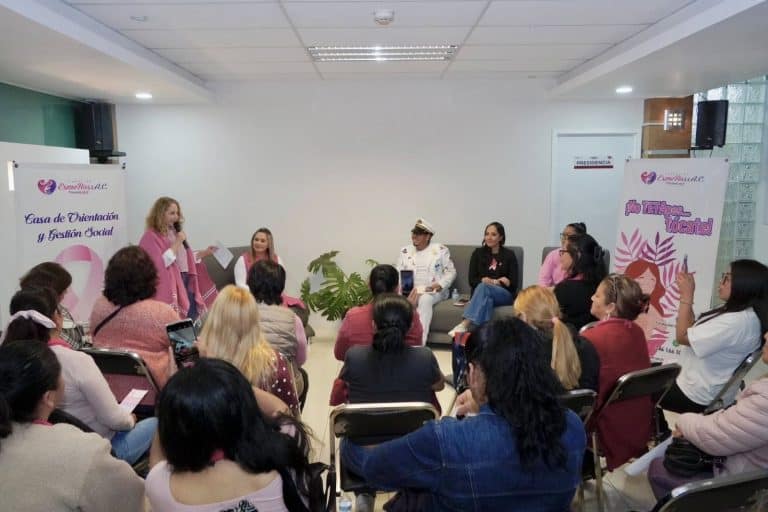 Mujer en vestido rosa hablando en panel de discusión con otras mujeres al fondo, en un evento de sensibilización sobre la violencia de género, en Tlaxcala, México.