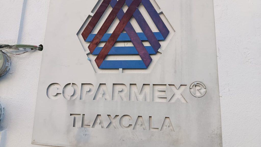 Firma de COPARMEX Tlaxcala en metal en color gris con logotipo en relieves y letras grabadas.