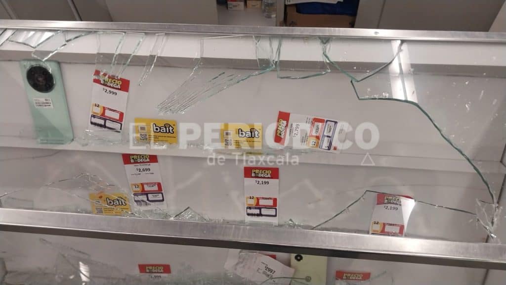 Vidrio roto en una exhibición de tienda con etiquetas de precios y un teléfono móvil.