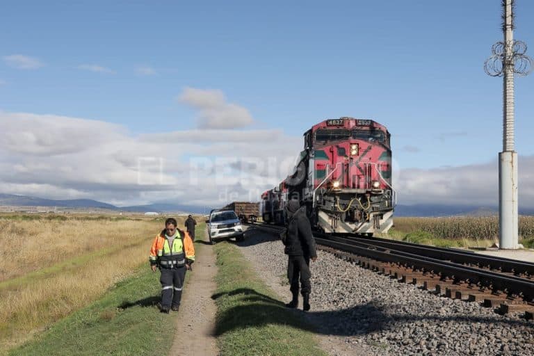 Vagones del tren en movimiento en medio de un campo, con personal de emergencia y un vehículo detenido cerca de las vías, bajo un cielo parcialmente nublado en Tlaxcala, México.