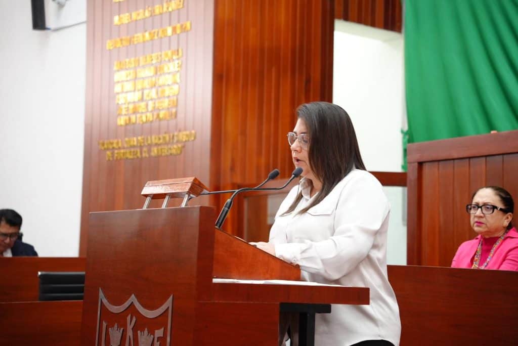 Diputada de Tlaxcala durante sesión en el Congreso estatal con fondo de madera y letras doradas.