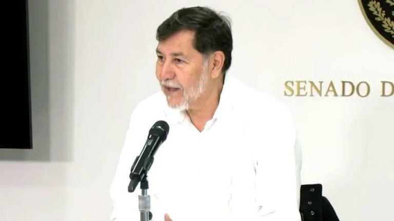 Diputado en conferencia en el Senado de México, vestido de blanco y con barba gris, durante una reunión oficial, frente a un fondo con logotipo y la palabra "SENADO".