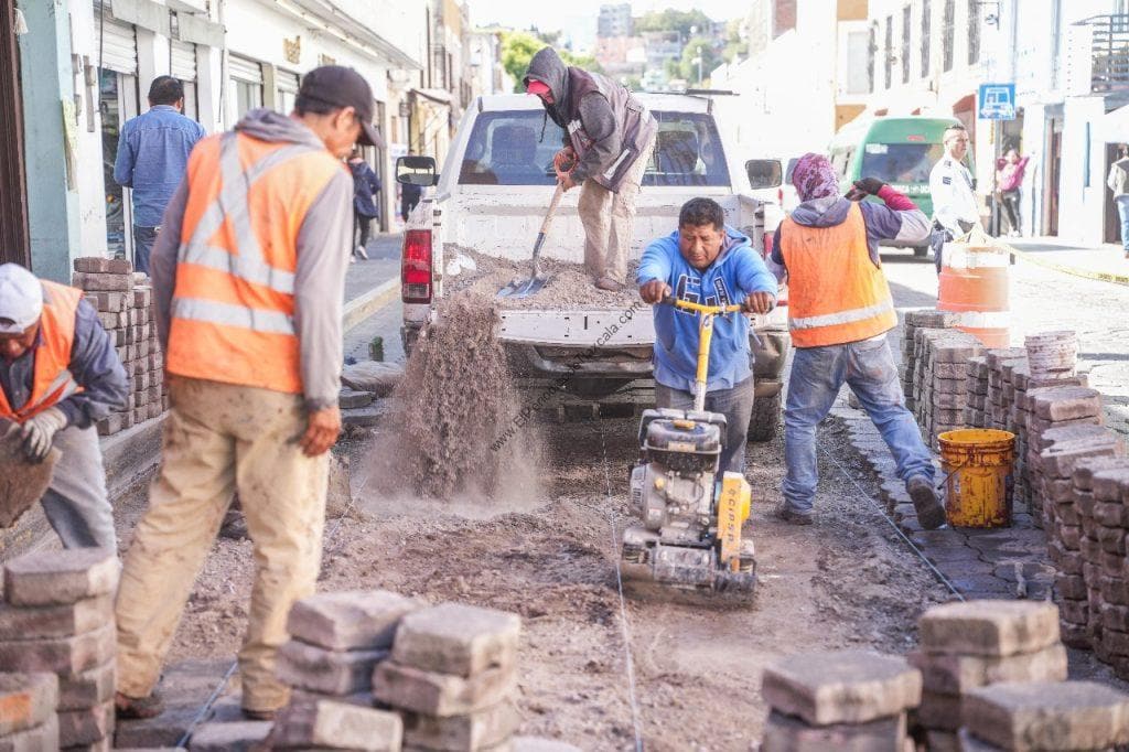 Trabajadores con equipo de seguridad reparan pavimento en calle de Tlaxcala, México, durante obra de construcción de banquetas y calzadas. Es un día de trabajo en la ciudad.