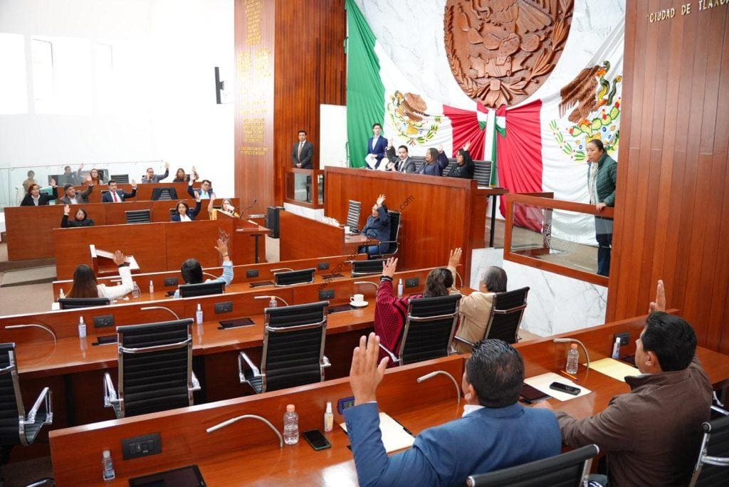 Diputados en sesión del Congreso de Tlaxcala con banderas nacionales y de Tlaxcala, participando en votaciones y debates sobre temas legislativos.