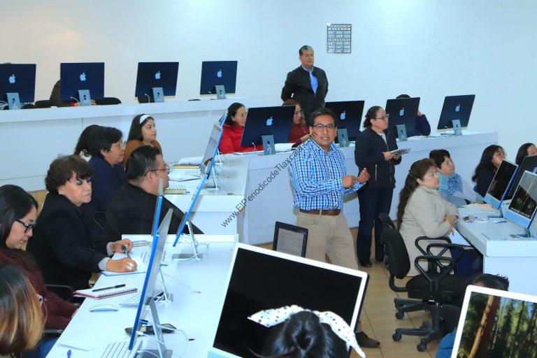 Personas en un taller de computación en un salón con computadoras Apple, algunos tomando notas, otros concentrados en las pantallas.
