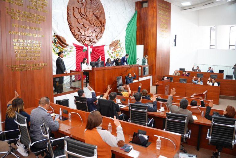 Diputados en sesión de pleno en el Congreso de Tlaxcala con la bandera nacional y el escudo en el fondo, discutiendo y votando temas legislativos importantes.