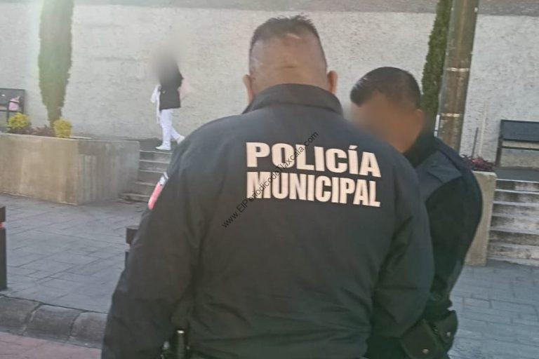Policías municipales en una calle de Tlaxcala, con dos oficiales de espaldas y uniformes negros con "POLICÍA MUNICIPAL" en la espalda, en un ambiente urbano con plantas y un muro de fondo.