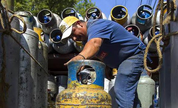 Tanque de gas llenándose en un mercado, con otros cilindros de gas en el fondo, listos para distribución o venta.