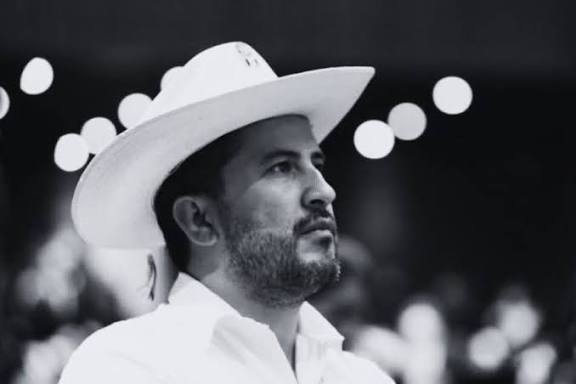 Hombre con sombrero blanco en un entorno oscuro, expresando serenidad y reflexión.