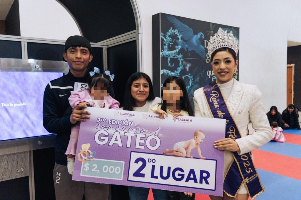 Premio a la segunda lugar en el concurso de gateo en Tlaxcala, entregado por autoridades locales durante evento infantil en un lugar cerrado con niños y adultos.