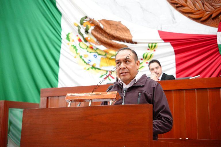 El hombre en el podio con bandera de México en el fondo, dando un discurso en un acto oficial.