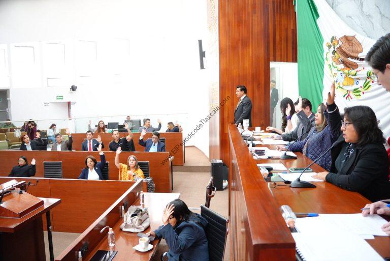Jurado en sesión en un parlamento, con varias personas levantando la mano durante una votación, en un entorno formal y con bandera de México en el fondo.