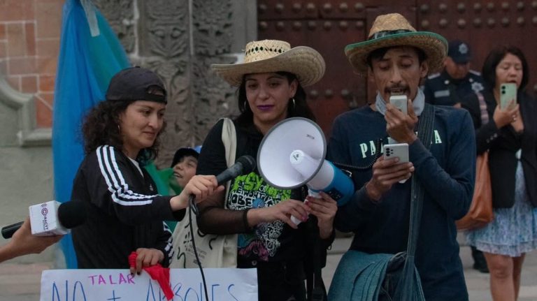 Abogada con sombrero y megáfono participando en una protesta en Tlaxcala, México, junto a otras personas que también usan sombreros y sostienen teléfonos móviles en una manifestación pública.