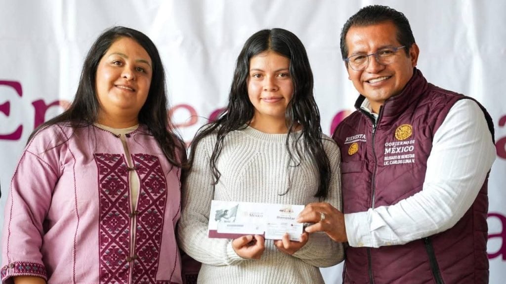 Ingreso de mujer recibiendo apoyo del gobierno, acompañada por dos funcionarios, en evento oficial en Tlaxcala, México.