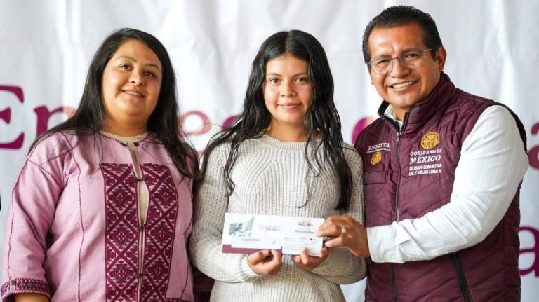Ingreso de mujer recibiendo apoyo del gobierno, acompañada por dos funcionarios, en evento oficial en Tlaxcala, México.