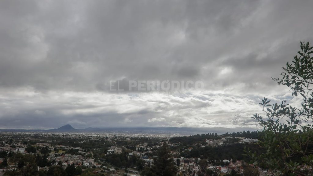 Nuboso cielo sobre la ciudad con montañas en la distancia y árboles en primer plano, ambiente de día nublado en Tlaxcala, México.