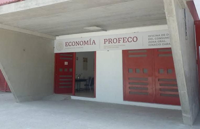 1. Oficina de Profeco en Tlaxcala con señalización para economía y consumo, en un edificio con estructura moderna y puertas rojas.