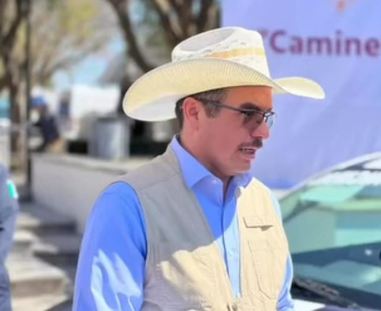 1. Hombre con sombrero y gafas, usando camisa azul y chaleco, en un entorno urbano con árboles y vehículos al fondo.