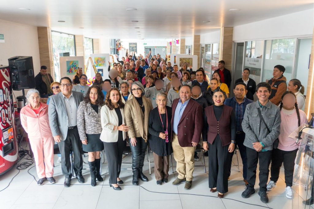 1. Grupo de personas en evento cultural o reunión en un espacio interior con arte en las paredes y público en el fondo.