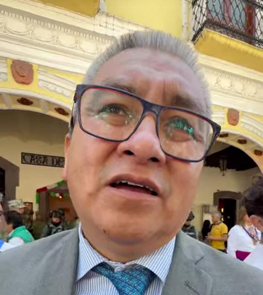 1. Hombre con gafas y traje en un entorno cultural y arquitectónico clásico en Tlaxcala con fondo de edificio histórico y detalles ornamentales.