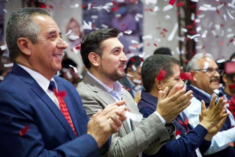 Consentimiento y celebración en un evento formal con asistentes aplaudiendo, vestimenta formal, confeti en el ambiente, ambiente festivo, reconocimiento a logros, ambiente de éxito y unidad.