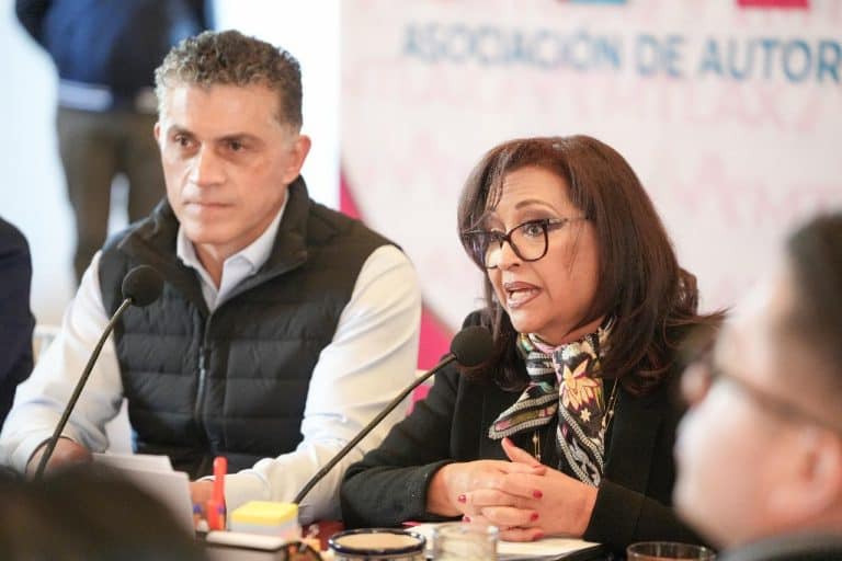1. Mujer y hombre en reunión formal, hablando en un foro o conferencia, con micrófonos frente a ellos, fondo con logotipo y texto en español, ambiente profesional.