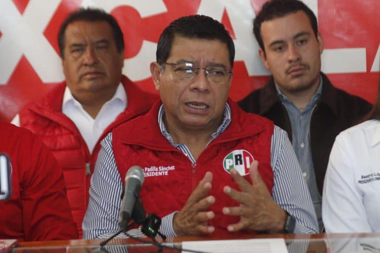 Diputado en conferencia de prensa con el logo del PRD en el fondo, en un acto político.