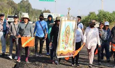 Una procesión con personas caminando y un estandarte religioso, en una actividad comunitaria en Tlaxcala, México.