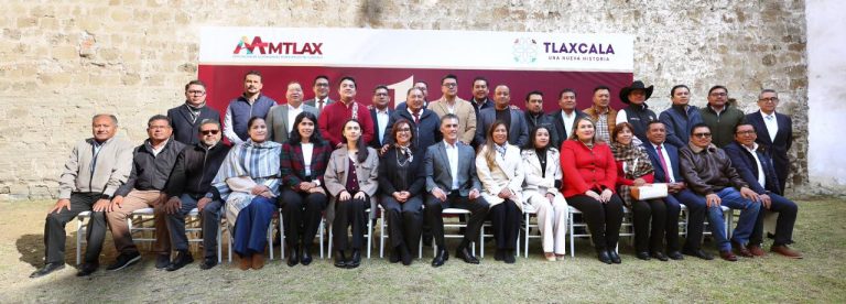 1. Grupo de líderes y representantes en evento de Tlaxcala con logos de AMTLAx y TLAXCALA en fondo de muro de ladrillos.