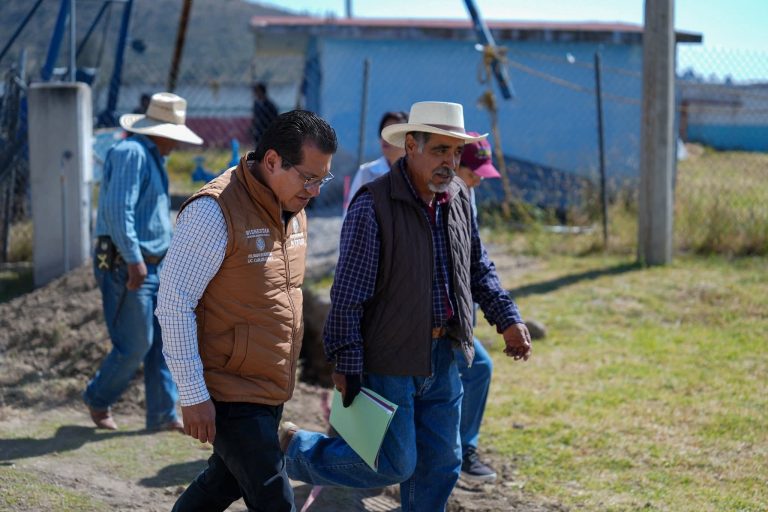 Asistentes con sombreros visitan una obra en un espacio abierto, observando y hablando con atención, en un día soleado en Tlaxcala, México.
