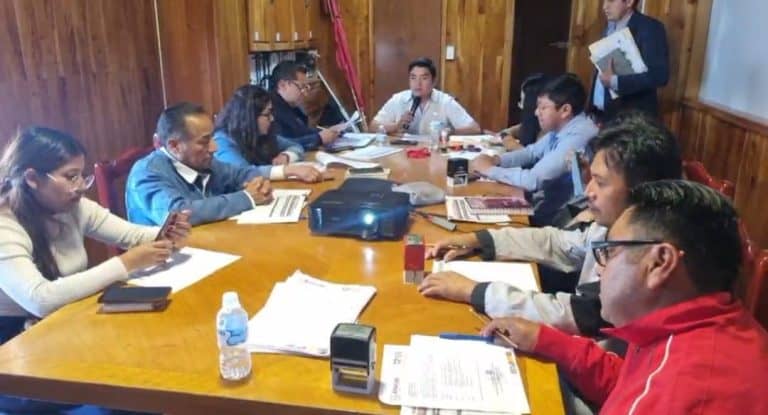Junta de trabajo con funcionarios y líderes comunitarios en Tlaxcala para definir acciones y acuerdos en temas de interés local. Participan varias personas en una reunión formal en un espacio cerrado de madera.