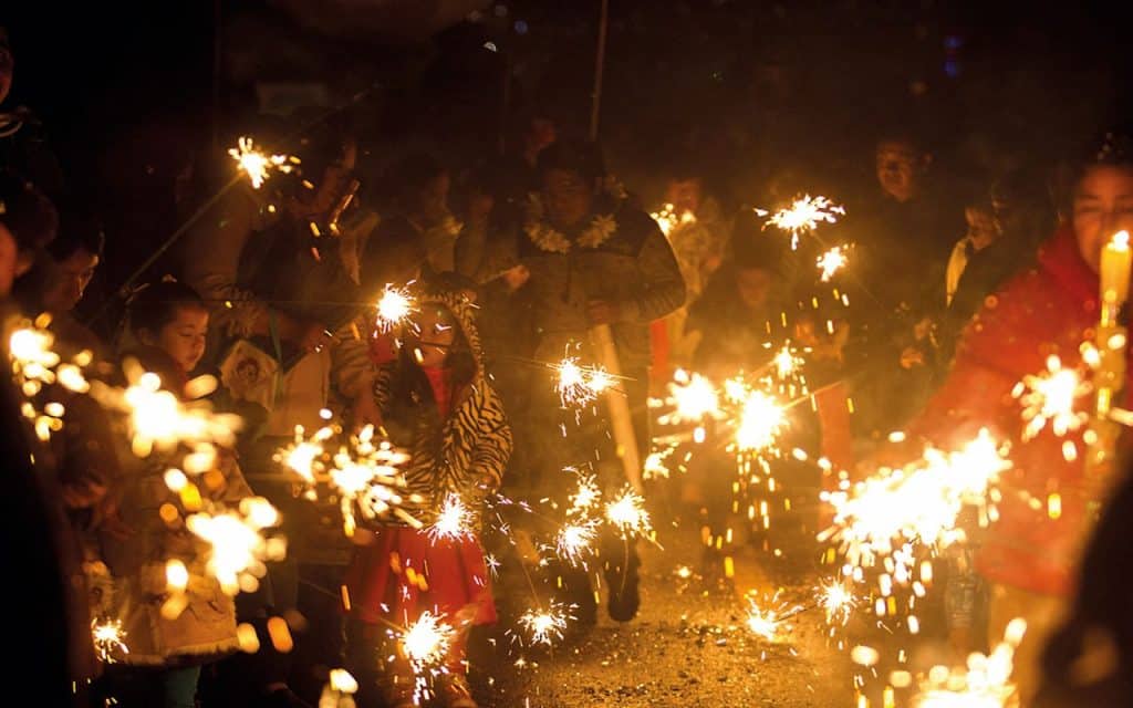1. Personas celebrando con fuegos artificiales durante una festividad en Tlaxcala, México, en la noche.
