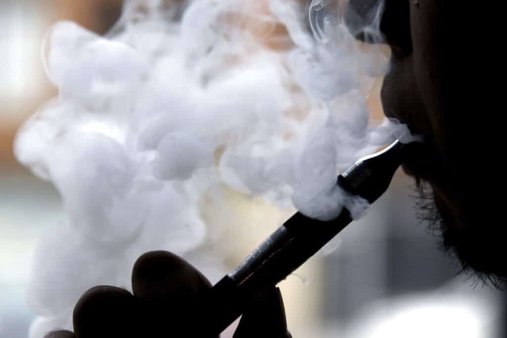 Contemplación de una persona usando un cigarro electrónico, con vapor visible en el aire, en un ambiente interior y oscuro.