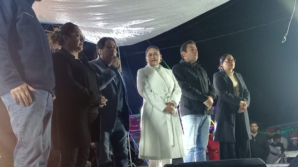1. Personas en un evento público al aire libre, algunos con expresiones serias, vestimenta formal y casual, en un escenario con decoraciones y luces.