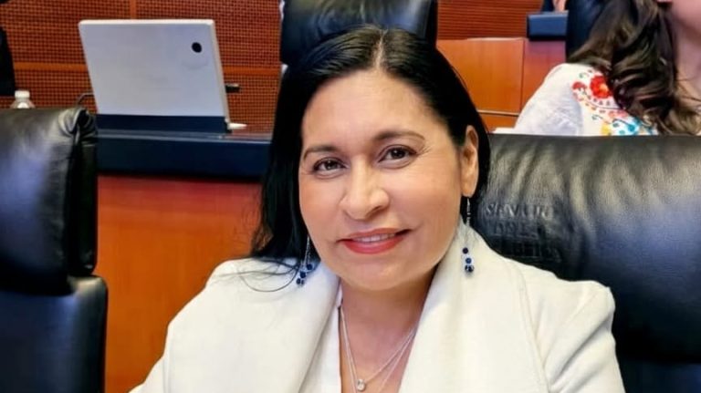 1. Mujer con cabello oscuro y sonrisa, sentada en una conferencia o reunión formal en un entorno profesional.