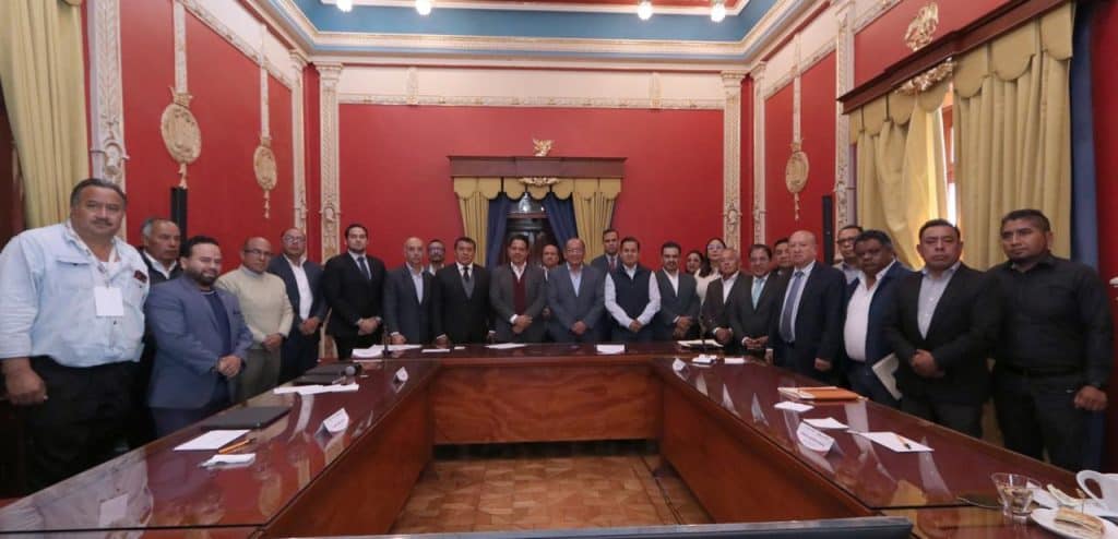 1. Grupo de profesionales en una sala de reuniones con paredes rojas y cortinas doradas, participando en un evento formal de discusión y toma de decisiones.