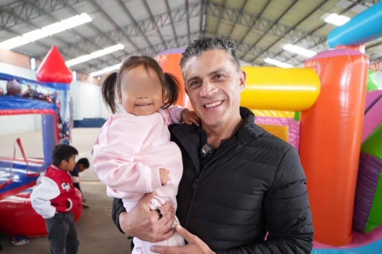 Disfrutando de un momento en un parque inflable, un hombre sonriente sostiene a una niña que también muestra felicidad, en un entorno cubierto con diversas estructuras de diversión para niños.