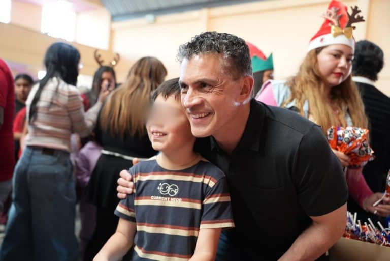 1. Un hombre sonriente abrazando a un niño en una celebración navideña con personas vestidas con gorros y accesorios festivos en un ambiente lleno de alegría.