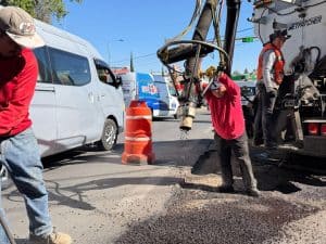 1. Trabajadores reparando una fuga de agua en una calle de Tlaxcala, en medio del tránsito vehicular, con maquinaria y señalización temporal.