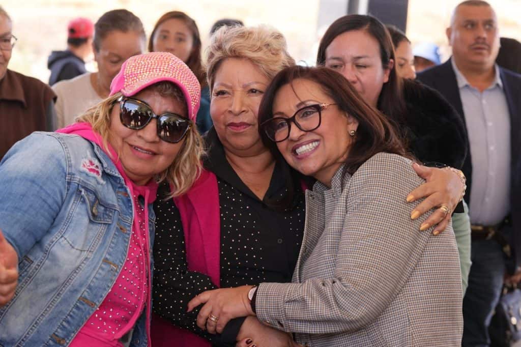 1. Mujeres abrazadas y sonriendo en un evento público con varias personas al fondo.